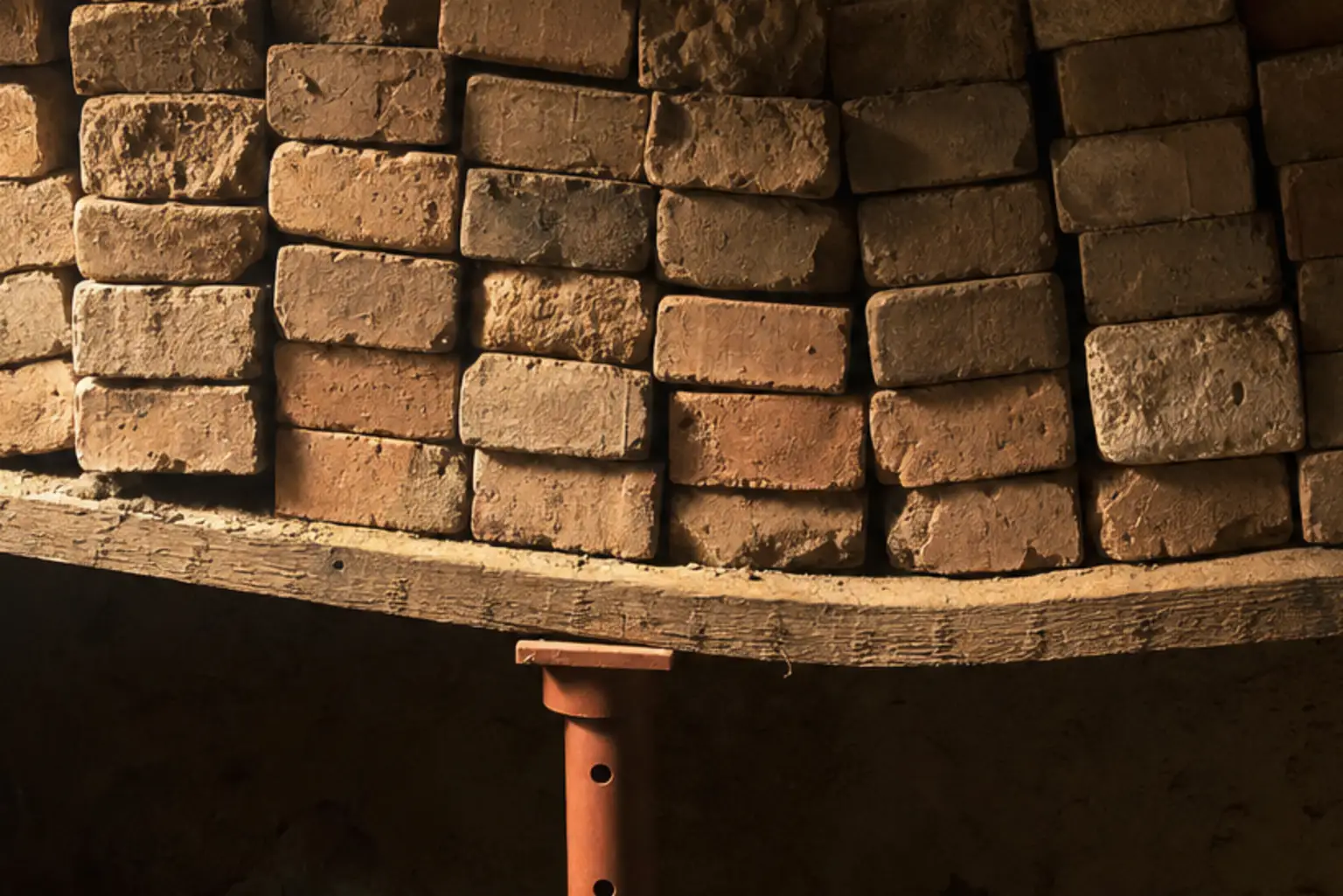 A shelf plank bowing under stacked bricks in a cellar light shaft, a fresh terracotta prop clamped beneath the worst of the bend.
